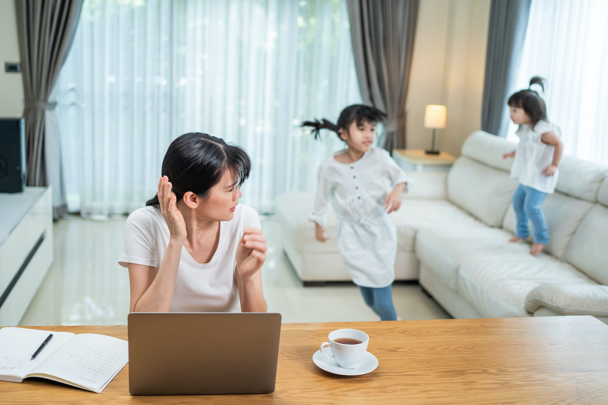 Asian businesswoman working at home due COVID-19 lockdown with children playing around.